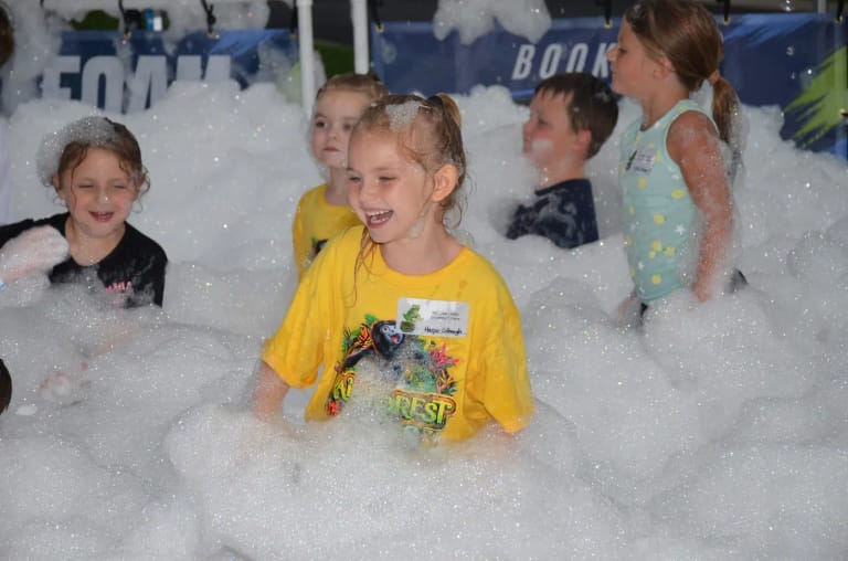 Kids playing in deep foam in front of the Elite Foam Experiences banner