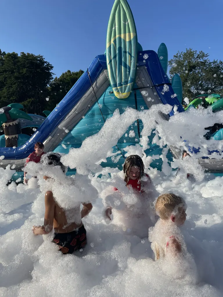 Kids waist-deep in foam beside a water slide at a summer foam party